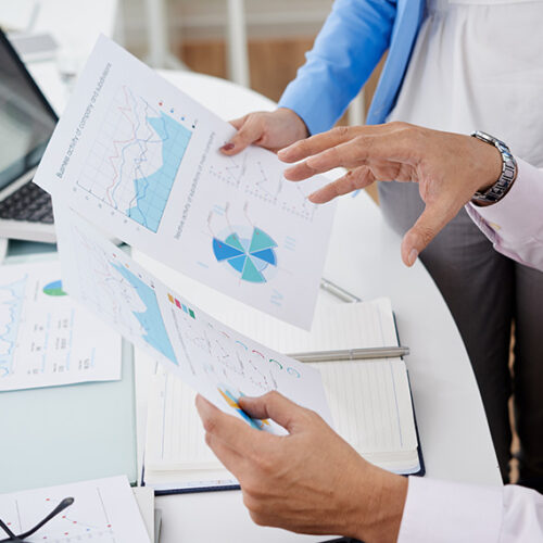 two business men reviewing print outs of finance charts at white desk