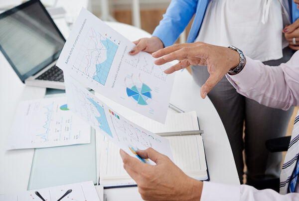 two business men reviewing print outs of finance charts at white desk