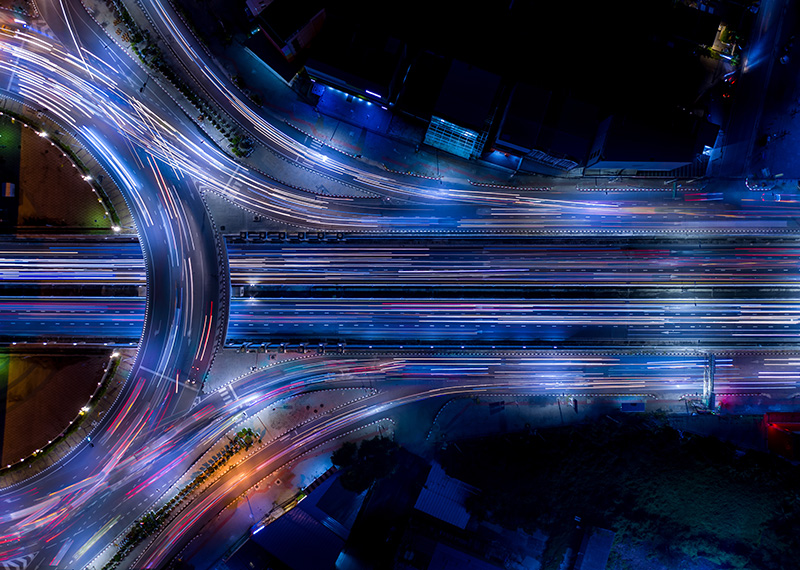 Birdseye view of highways intersecting at night with streak of car lights visible