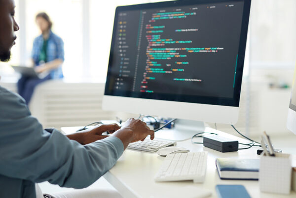 DevOps engineer typing on a large monitor with code on the screen