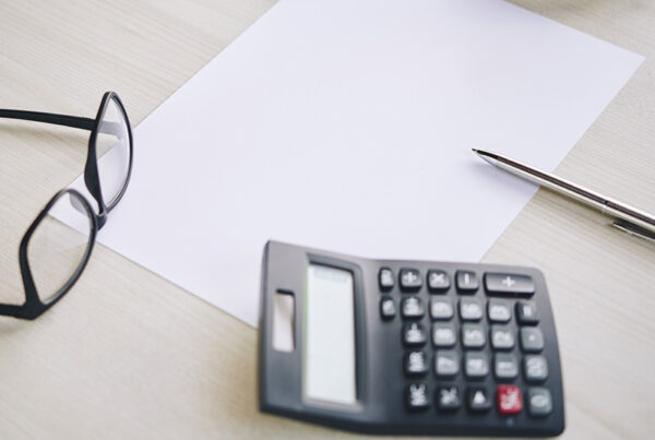 black calculator on a work desk with blank piece of paper, glasses, and pen