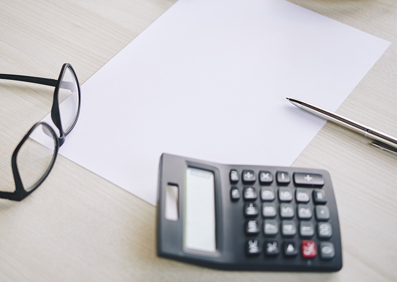 black calculator on a work desk with blank piece of paper, glasses, and pen