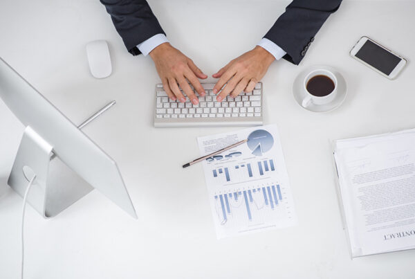aerial view of a business desk with hands on a keyboard, coffee, phone, and monitor