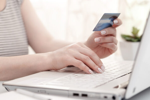 woman holding credit card and typing number into laptop