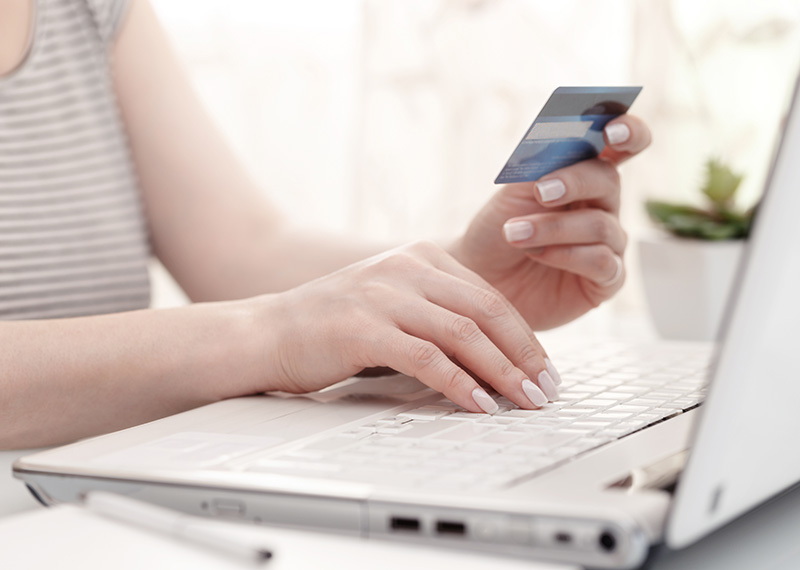 woman holding credit card and typing number into laptop