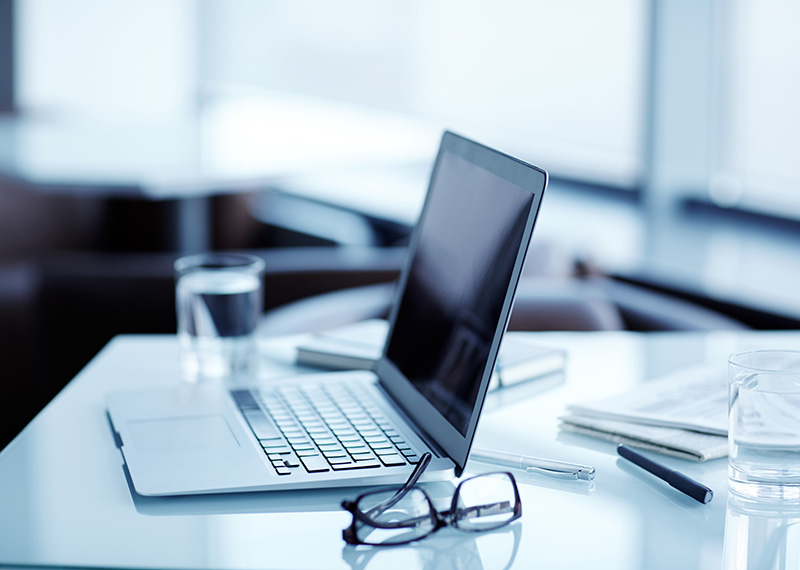 laptop on translucent desk with eye glasses and a glass of water