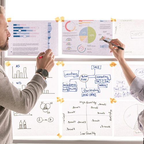 business man and woman reviewing financial charts taped to a translucent window that is backlit