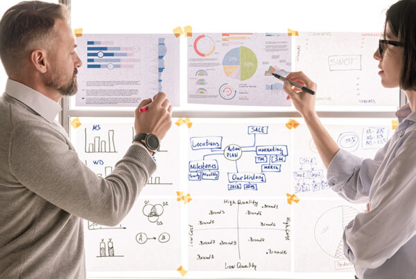 business man and woman reviewing financial charts taped to a translucent window that is backlit