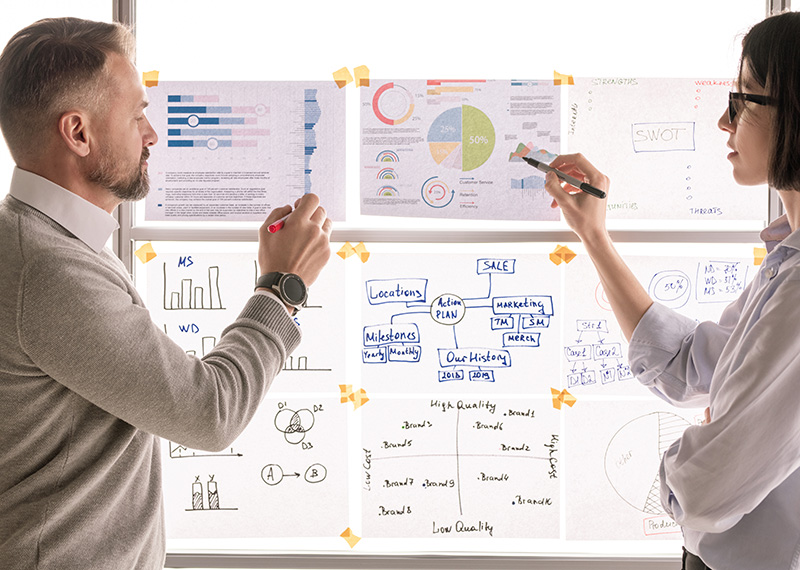 business man and woman reviewing financial charts taped to a translucent window that is backlit