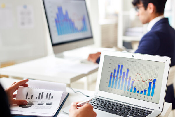 two sales operations analysts working in office with view of bar charts on their screens