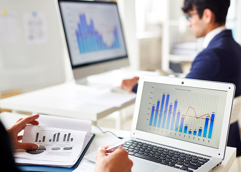 two sales operations analysts working in office with view of bar charts on their screens