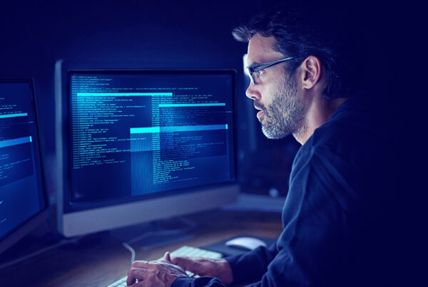 a software developer in darkly lit room viewing source code on two monitors