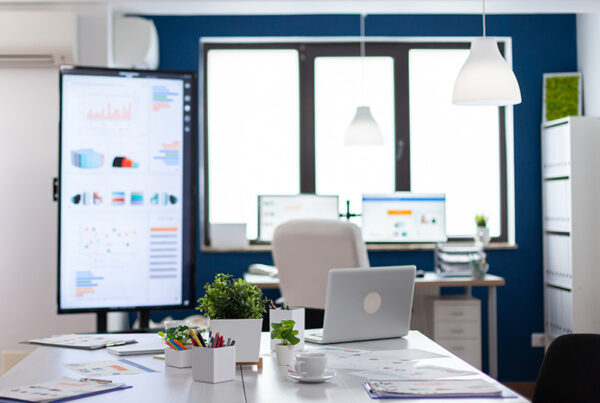 empty office with monitors, laptop on table, and windows in background