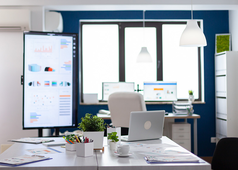 empty office with monitors, laptop on table, and windows in background