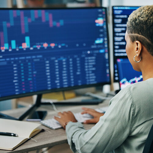 business woman sitting at office desk with monitors in foreground