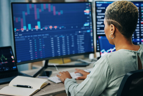 business woman sitting at office desk with monitors in foreground