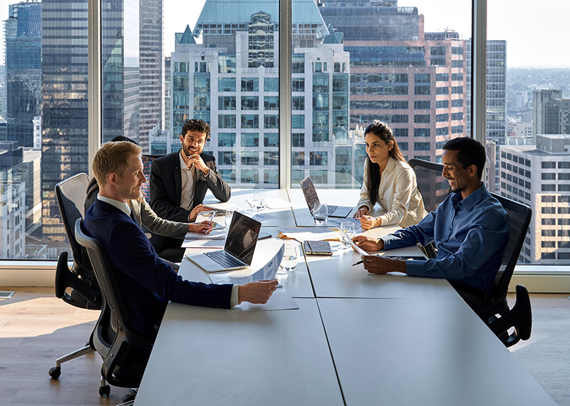 Vice President of sales sitting with customers at conference table with city skyline in background