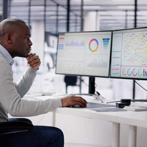 Financial analyst looking at two large monitors in office to identify revenue leakage
