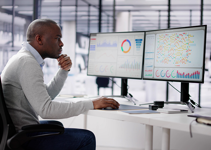Financial analyst looking at two large monitors in office to identify revenue leakage