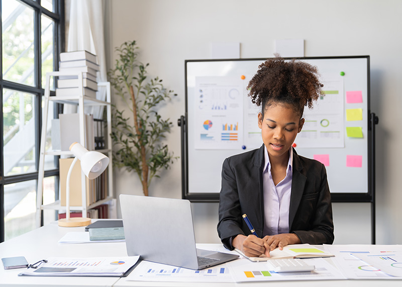 field marketing manager sitting in brightly lit office with laptop on desk and whiteboard in background