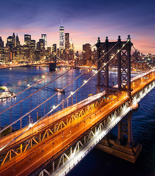View of New York City at sunset from across East River with Brooklyn Bridge in foreground
